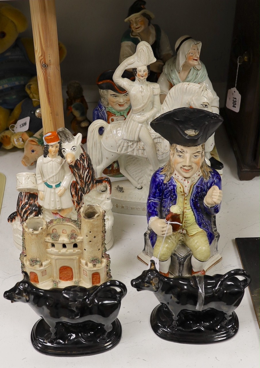 Five Staffordshire pottery figures or groups, tallest 36 cm high two similar Toby jugs, a pair of black glazed cow creamers and a model of a castle